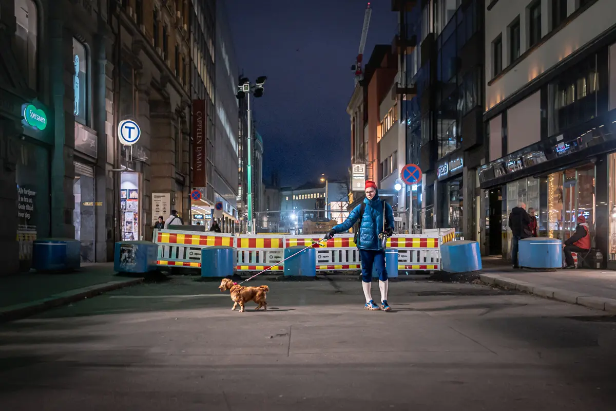 Norweian man walking his dog in a city side street wearing ski wear.