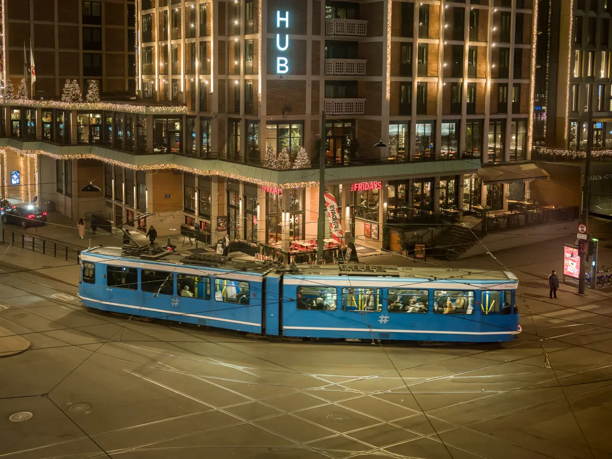 Bird's eye view of the SL79 tram car as it passes Europarådets plass at night. Yellow street lights contrasting the blue tram exterior.