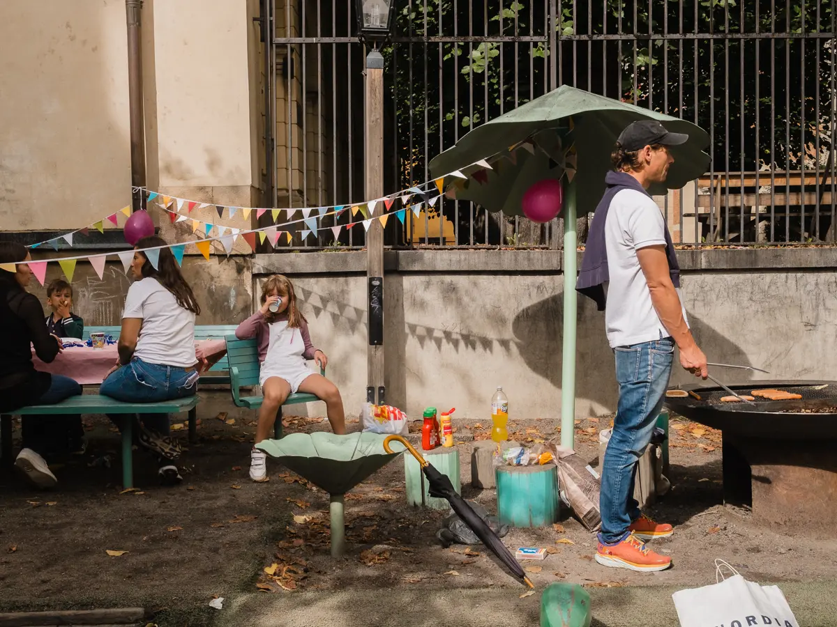 Family having a park birthday party. The father looking unenthusiastic as he is grilling the hot dogs.