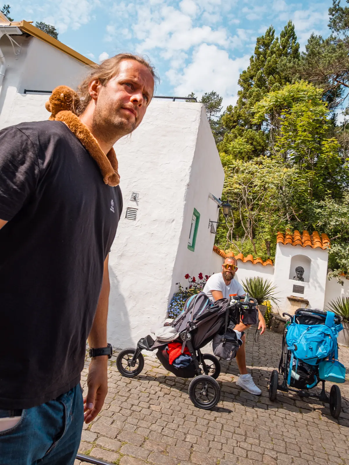 Two dads with strollers and stuffed animals at the zoo.