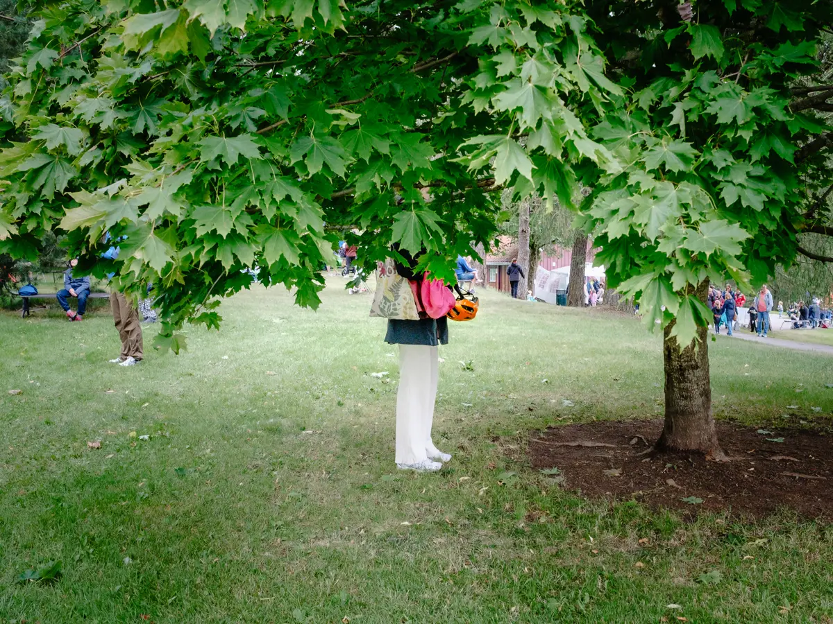 Woman with her upper half covered by the leaves of a low tree as she's waiting for her child to come down so they can go home.