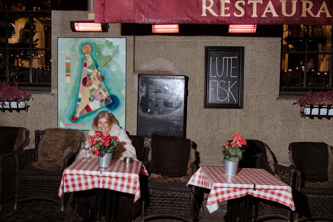 Exterior of Oslo restaurant Lorry with a chalkboard that reads Lutefisk. A woman sits at one of the outside tables meant for smokers in front of the wall.
