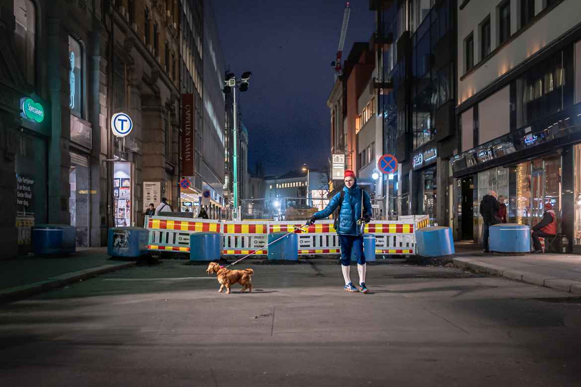 Norweian man walking his dog in a city side street wearing ski wear.