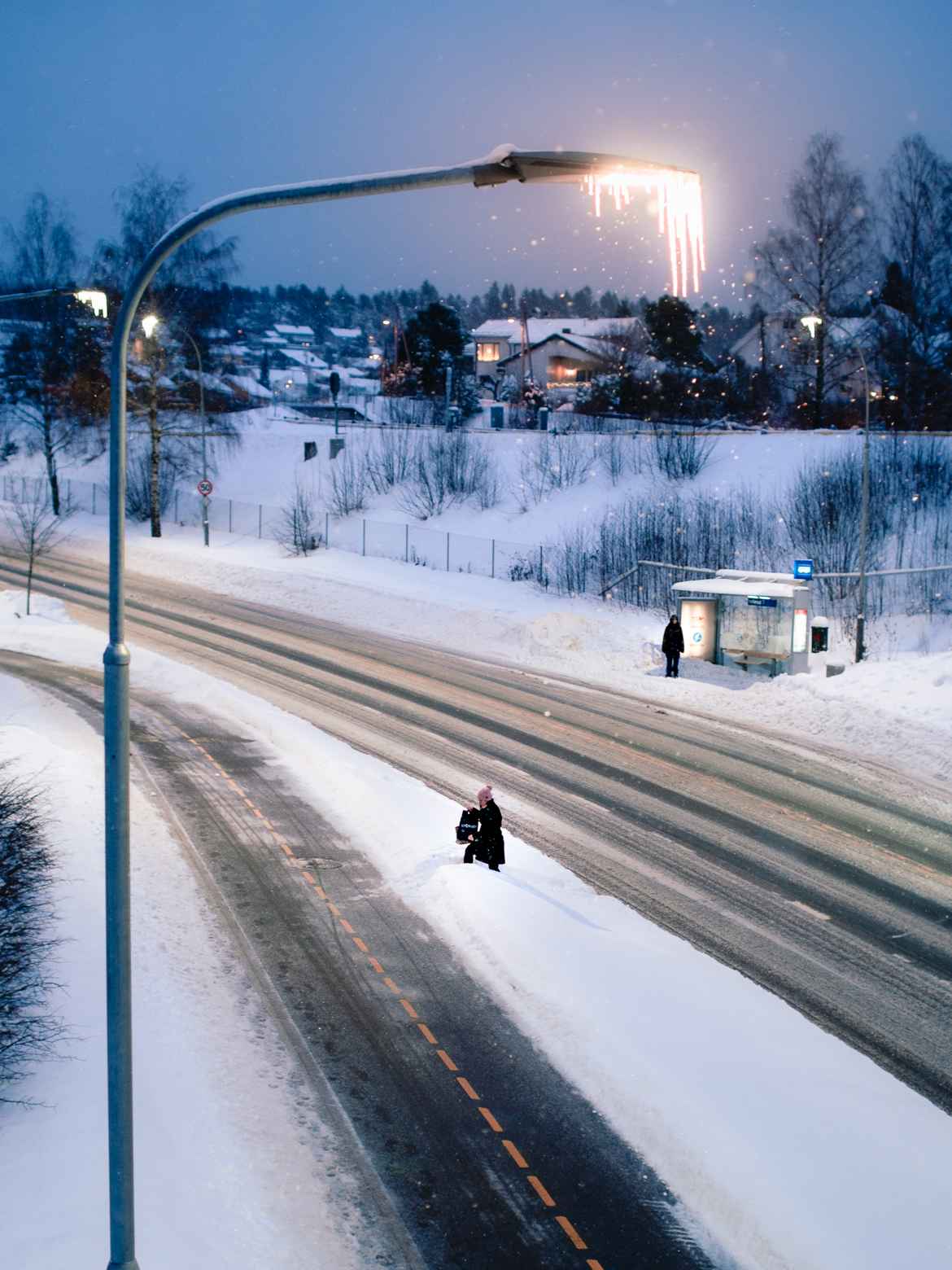 Woman in the distance, photographed from above while she attempts to climb over a massive plow edge between the road and the footpath.