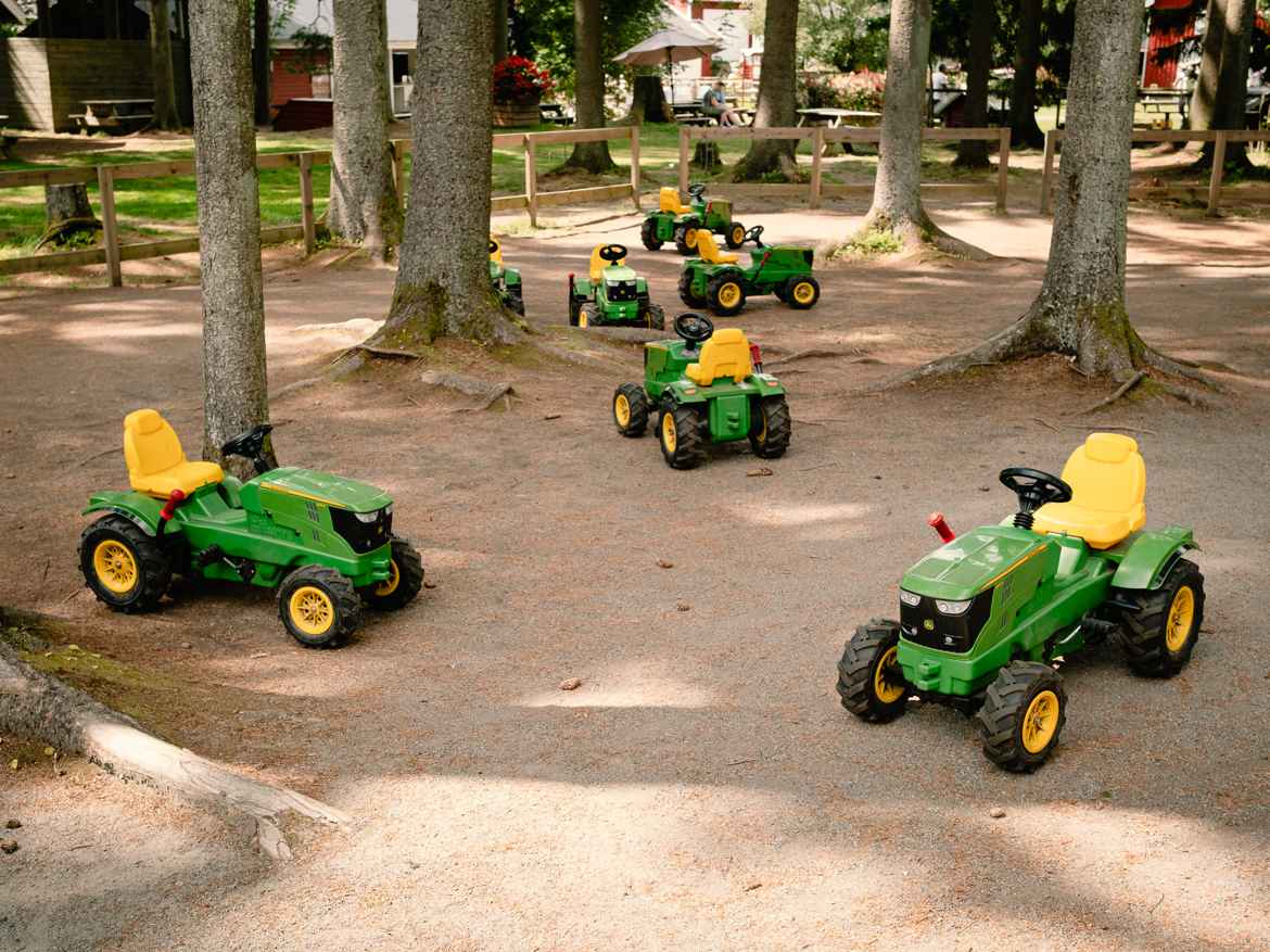 Yellow and green toy pedal tractors in the woods.