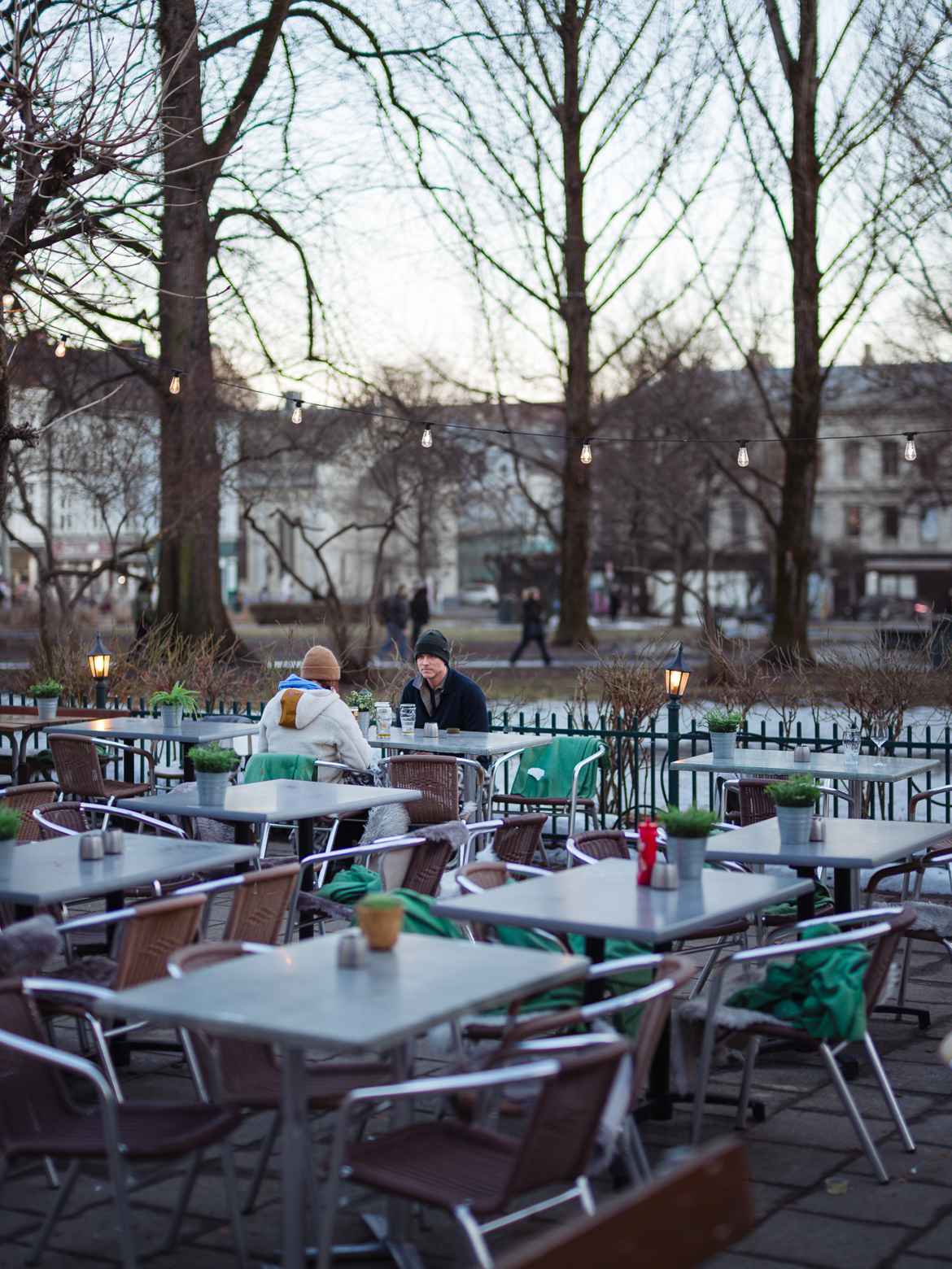 Couple in an otherwise empty outdoor restaurant trying to have a beer outside without freezing too much.