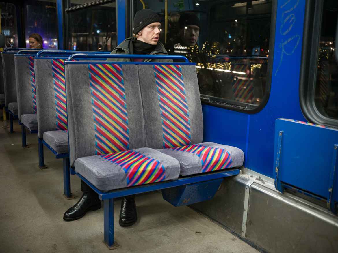 Young man seated alone on the back left isle of seats, on the second row. Only his head and feet are visible. His feet sticking out under the seats. Seems like the tram is designed for shorter people than him.