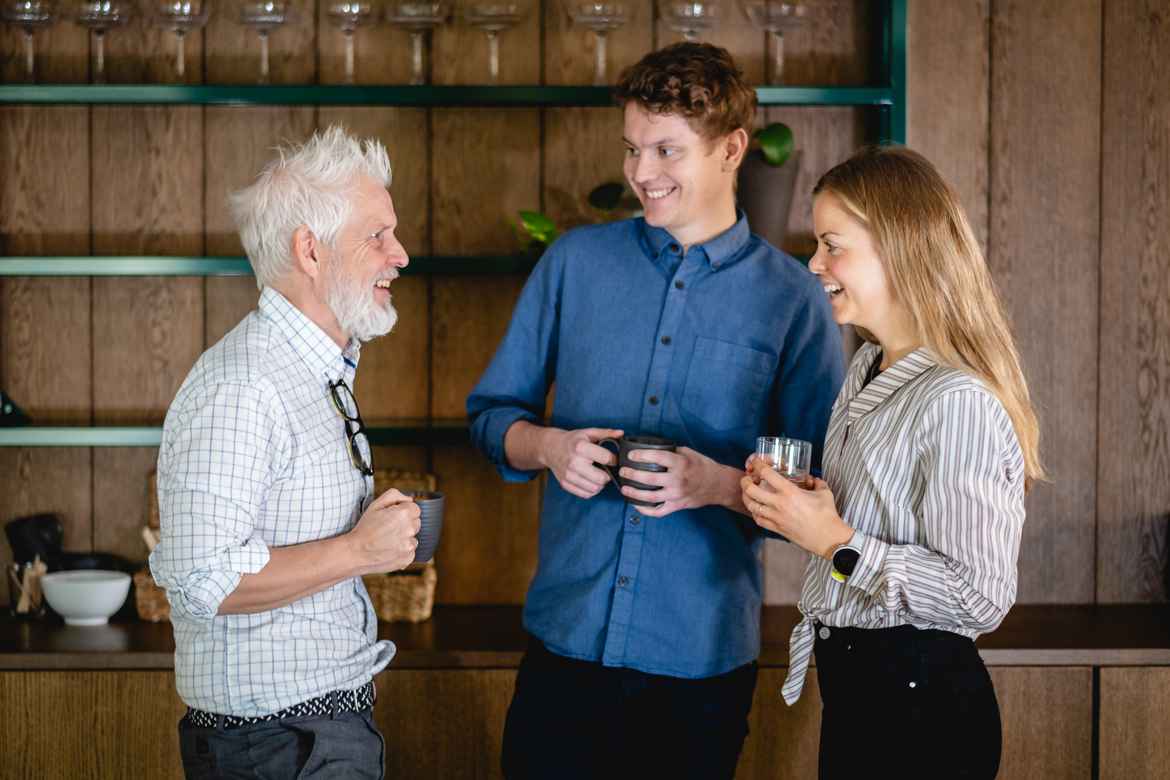 Colleagues, two younger and one senior man talking in the office kitchen.