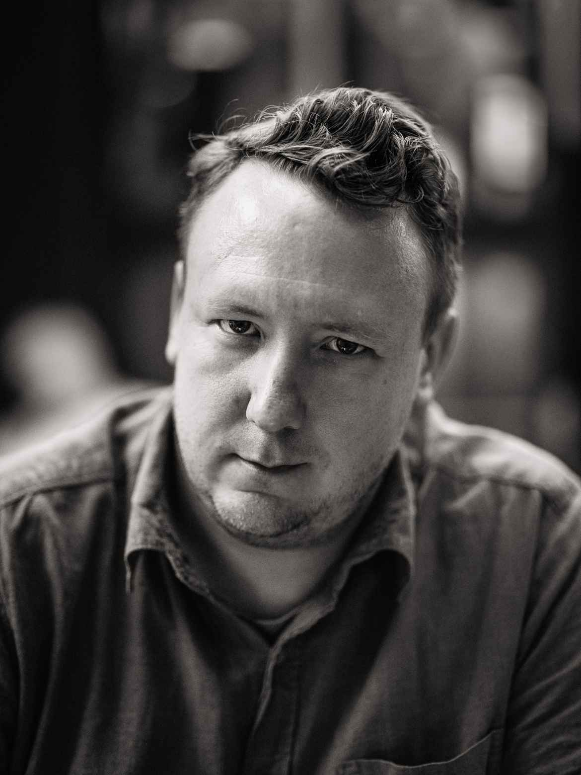 Black and white image of Photographer Andreas Feydt. Mid-torso, head leaning forward with a strong gaze straight into the camera.