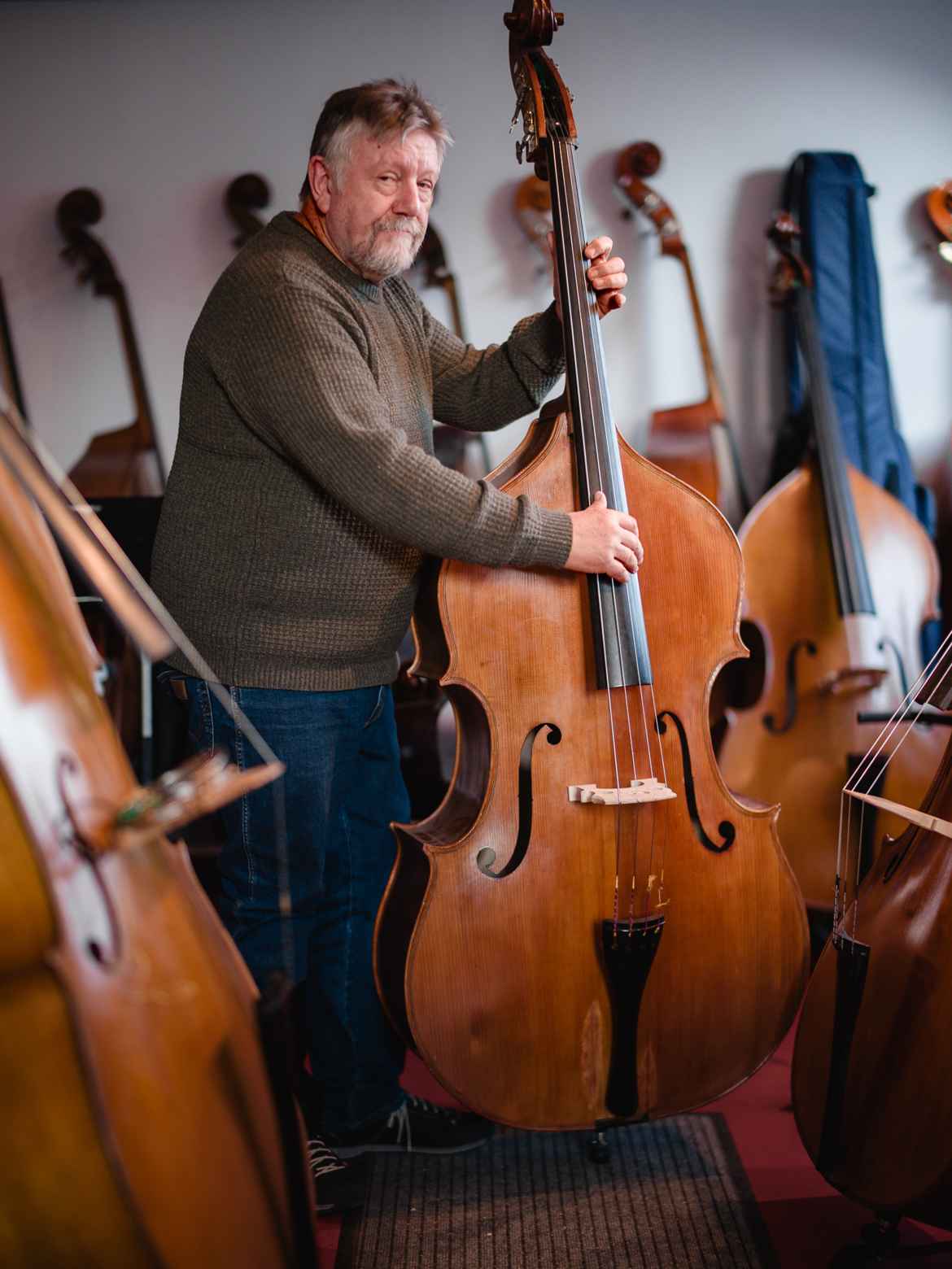 Helge Ellingsen in his bass shop surrounded by upright basses, holding one and playing.