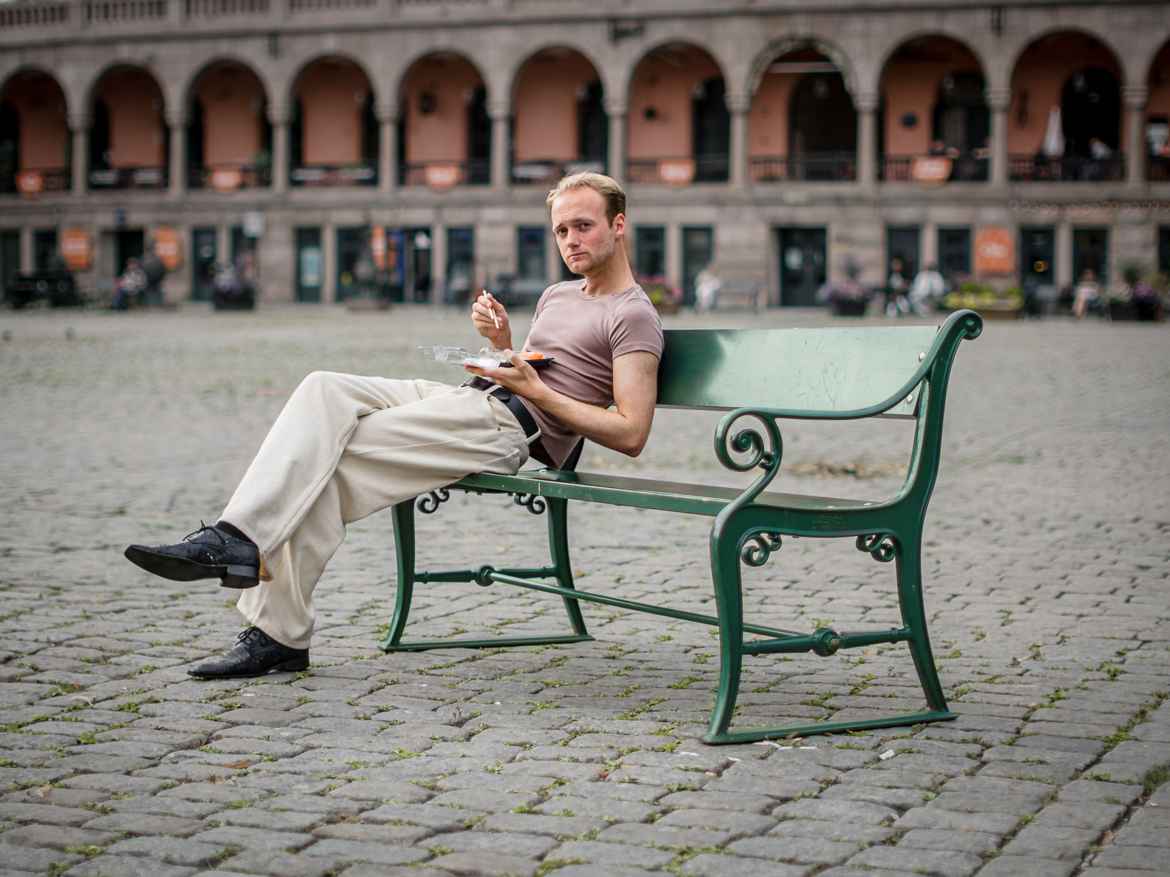 Young man wearing muted colors having sushi on a green bench at Youngstorget.