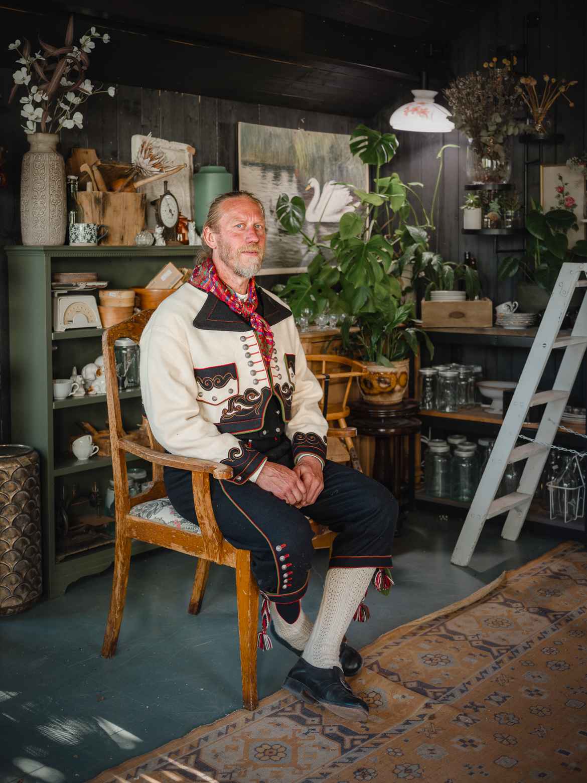 Marius Andersen sitting in an old, wooden chair wearing traditional Norwegian bunad in a country style decorated room.