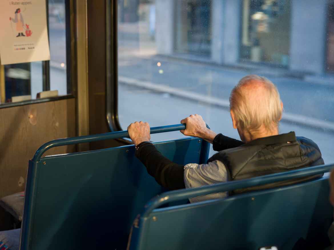 Elderly man grabbing on to the seat row in front of him on the tram, like he is riding a rollercoaster.