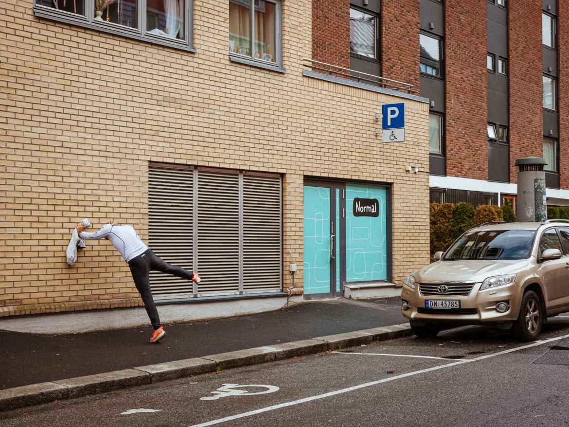 Man leaning agains a brick wall in a strange pose looking like he is stretching.