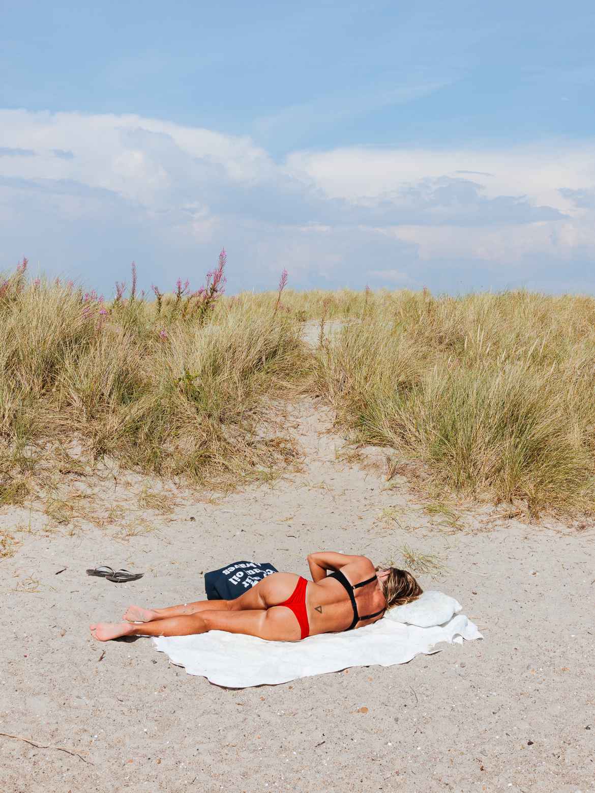 Womain in red bikini on beach, sleeping on a white towel in the sand.