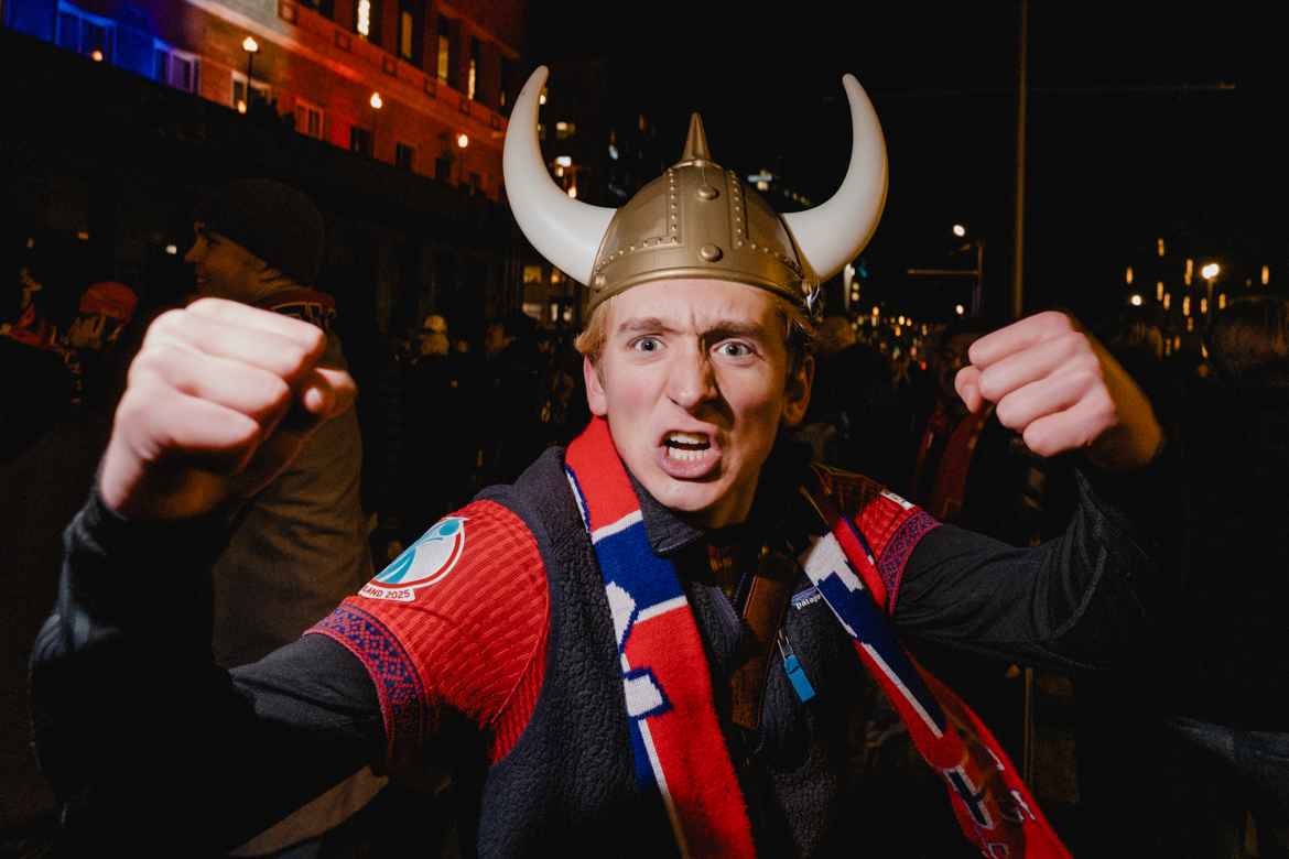 Young man in plastic viking helmet and Norwegian national soccer scarf making fists at the camera in celebration of Norway qualifying for the 2026 football world cup.